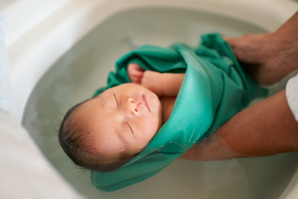 bébé nouveau né dans son bain photographié par Marie Cavelier lors d'une séance naissance à versailles à domicile